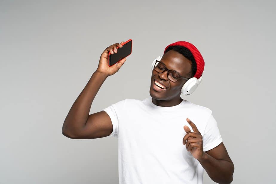 African American man with headphones enjoying listening to music, dances, holding mobile phone