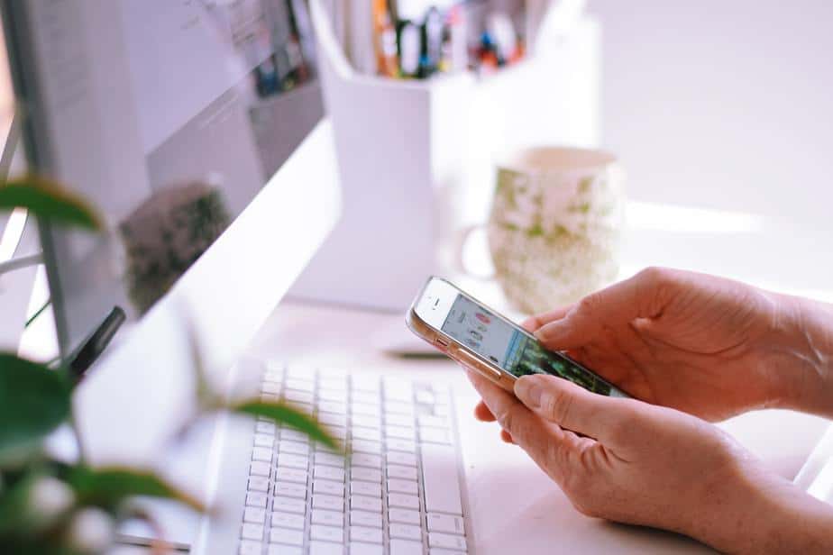 Woman sitting at a desk in home office in front of a computer and browsing Instagram on mobile phone